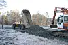 En dumperhenger har tippet et lass med pukk på det som skal bli en skogsvei over ei myr. Ei gravemaskin står klar til å spre den utover.