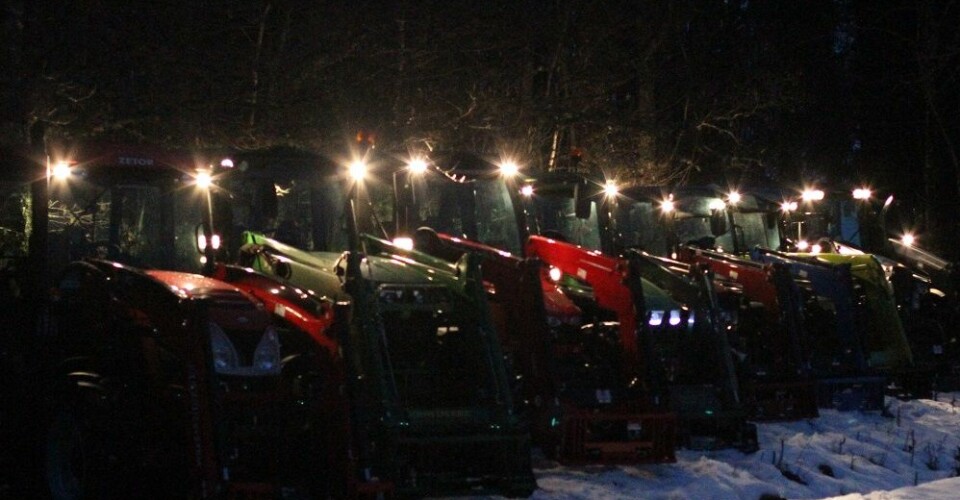 Åtte traktorer på rekke og rad med lysene på i vinternatta.