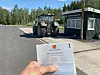 I forgrunnen: Ei hånd som holder opp et vognkort. I Bakgrunnen: En traktor på vekta på en kontrollstasjon.
