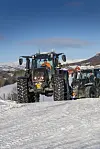 To valtra traktorer på vei opp en snødekt bakke i Oppdal med blå himmel i bakgrunnen