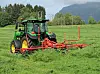 John Deere traktor med ei rød rive bak på et grønt jorde