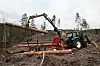 Traktor med tømmerhenger med kran ute i et hogstfelt og laster opp tømmerstokker