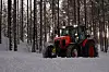 En Kubota traktor ute i en snødekt skog med en freser bakpå