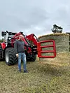Audun Aaserud poserer ved siden av en Massey Ferguson traktor med en rød rundballeklype fra Lilleseth Redskap som holder en rundballe