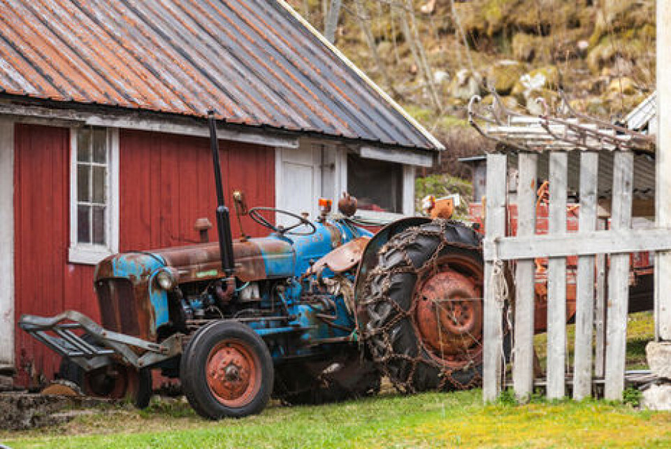 Eldre, slitt traktor parkert utenfor en rødmalt bygning