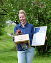 Silje Maria Kvaale By holder en melkekrakk, blomster og et diplom i grønne omgivelser