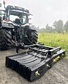 En traktor med et veislodd i ei kombiramme parkert på en grusveg