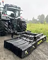 En traktor med et veislodd i ei kombiramme parkert på en grusveg