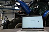 PC-skjerm stående i et traktorverksted med en New Holland traktor med åpent panser i bakgrunnen