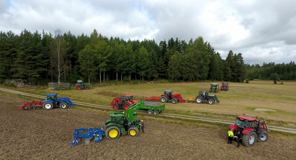 Ni trinnløse traktorer med ulike redskaper plasert ute på et jorde med journlister rundt i gang med å teste dem.