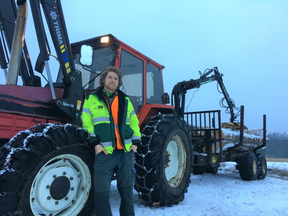Christoffer Askheim poserer foran traktoren med tømmerhenger bak.