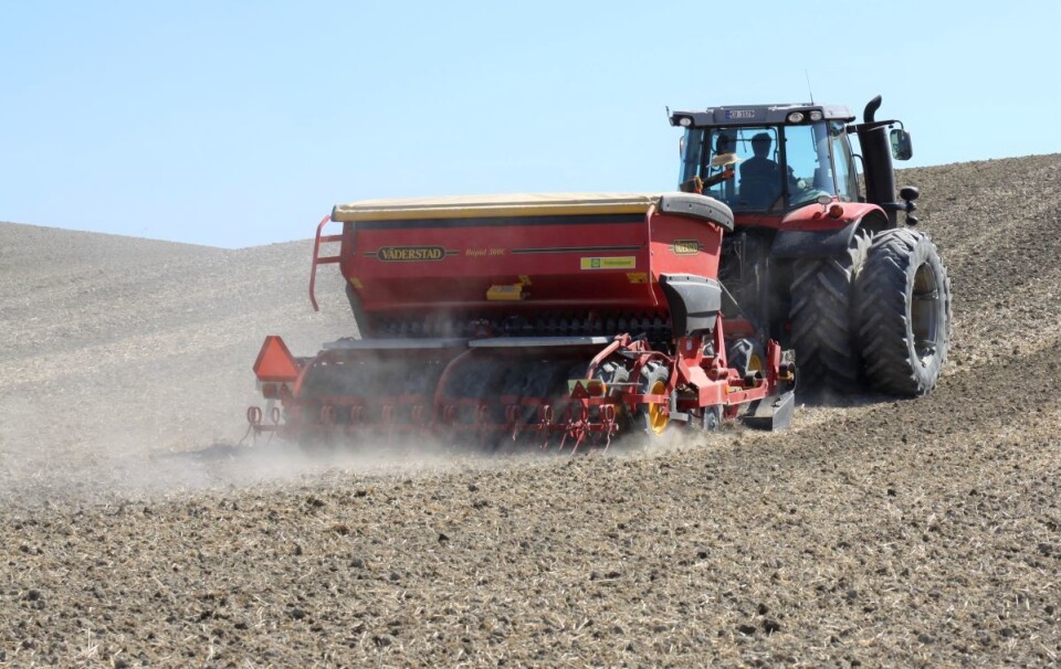 Traktor med tvillinghjul og en Väderstad såmaskin bak kjører over et tørt jorde på Romerike mens støvskya står bak.