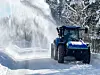 En blå traktor som brøyter snø ved hjelp av snøfreser.