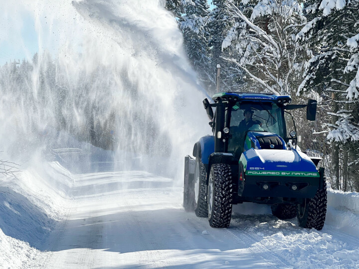 En blå traktor som brøyter snø ved hjelp av snøfreser.