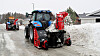 To metantraktorer fra New Holland kjører etter hverandre på en vei og brøyter snø ved hjelp av snøfresere