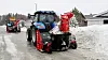 To metantraktorer fra New Holland kjører etter hverandre på en vei og brøyter snø ved hjelp av snøfresere