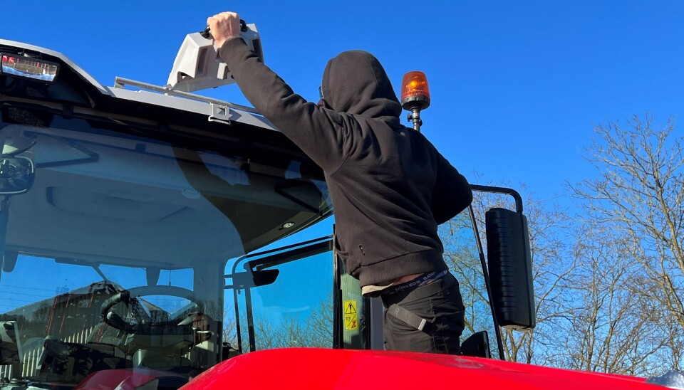 Mann i svarte klær og hette over hodet strekker seg etter en GPS-antenne på en Massey Ferguson-traktor.