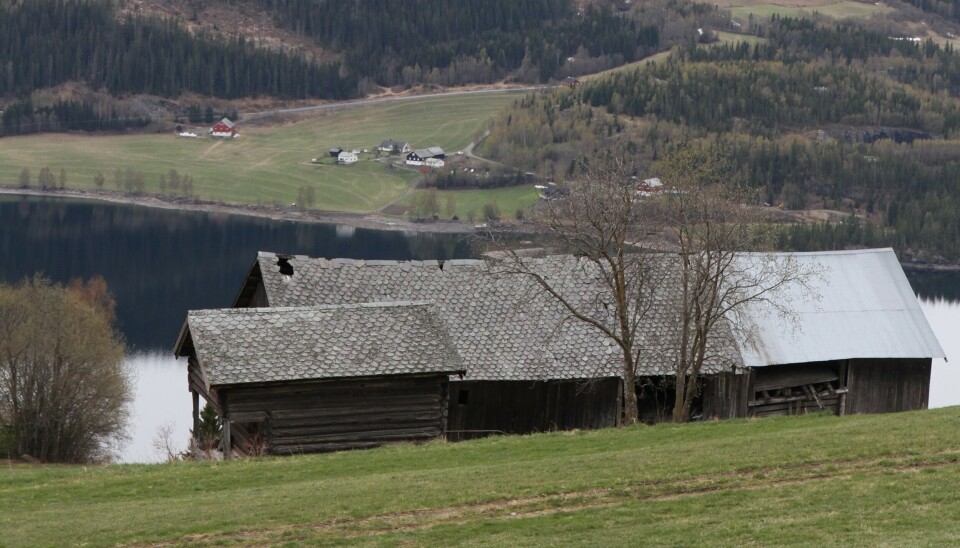 En eldre, forfallen driftsbygning oppe i fjellsida med utsikt over kulturlandskap og et vann.